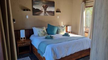 Un dormitorio con cama de madera, mesita de noche, lámpara de pared, un cuadro y una ventana con cortinas.