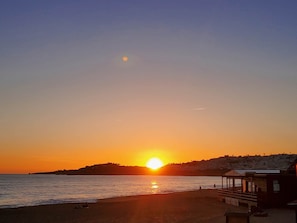 A beach scene with the sun setting over the water, a pier, and a hill in the background. - Beachfront Apartment - I (Albufeira)