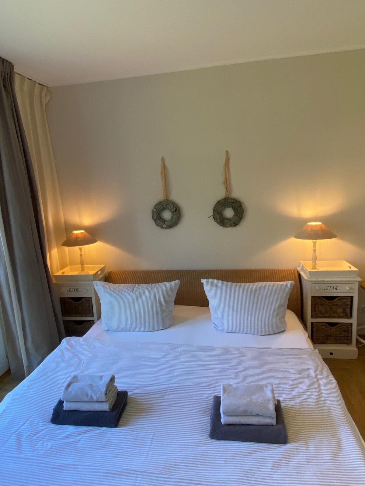 Un lit bien fait, avec deux oreillers, deux serviettes pliées et deux lampes fixées au mur, placées sur les tables de chevet.