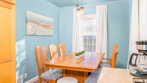 Un comedor con una mesa de madera, cuatro sillas, una cafetera y una ventana con cortinas.