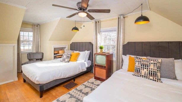 Un dormitorio con dos camas, ventilador de techo, televisor y ventana con cortinas.