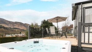 A hot tub with a view of mountains, outdoor furniture, and a patio area. - Red Kite Lodge (Crieff)