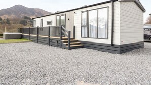 A small, single-story mobile home with a deck and a hot tub. - Red Kite Lodge (Crieff)