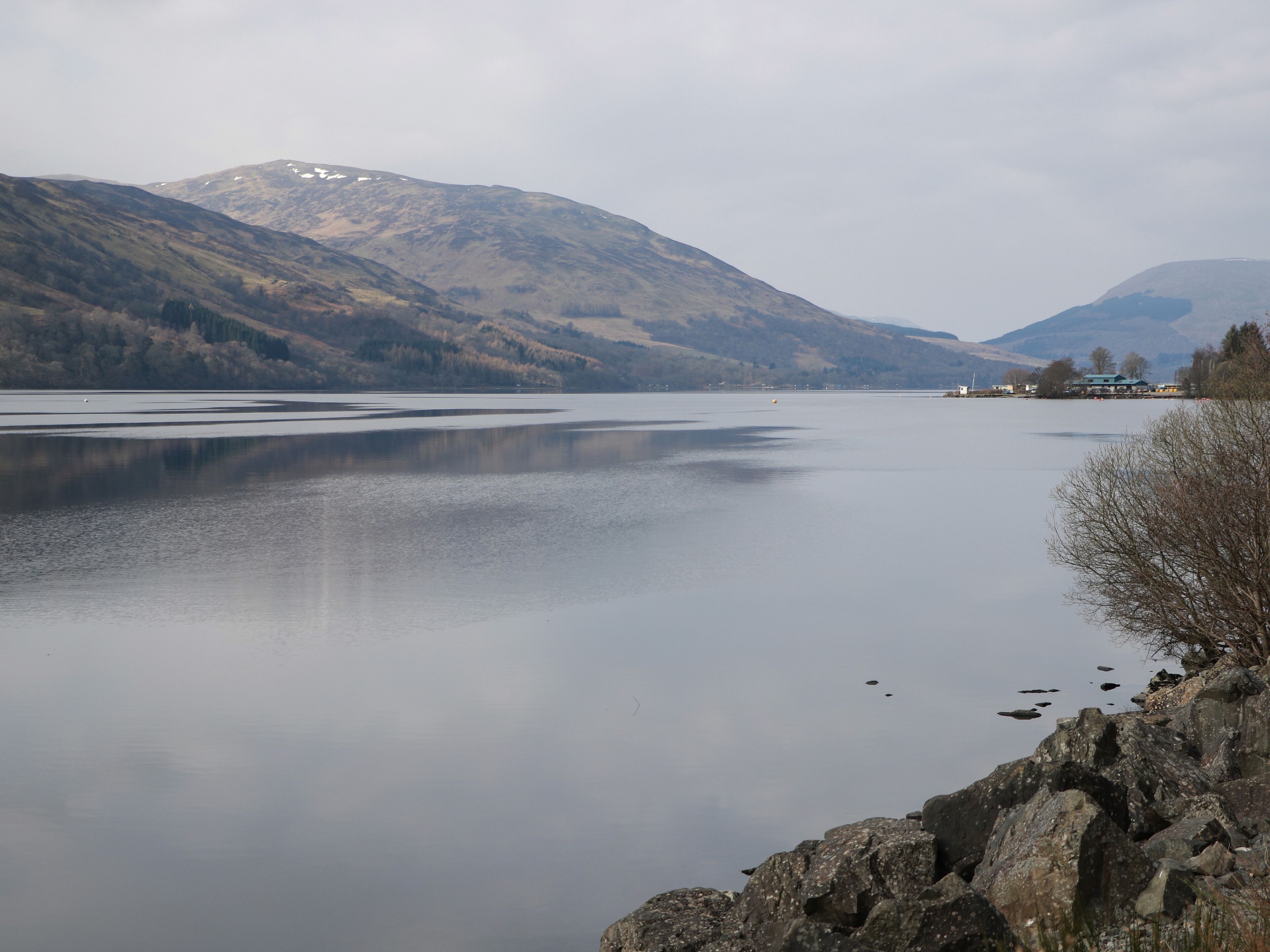 A calm lake with mountains in the background and a rocky shoreline.