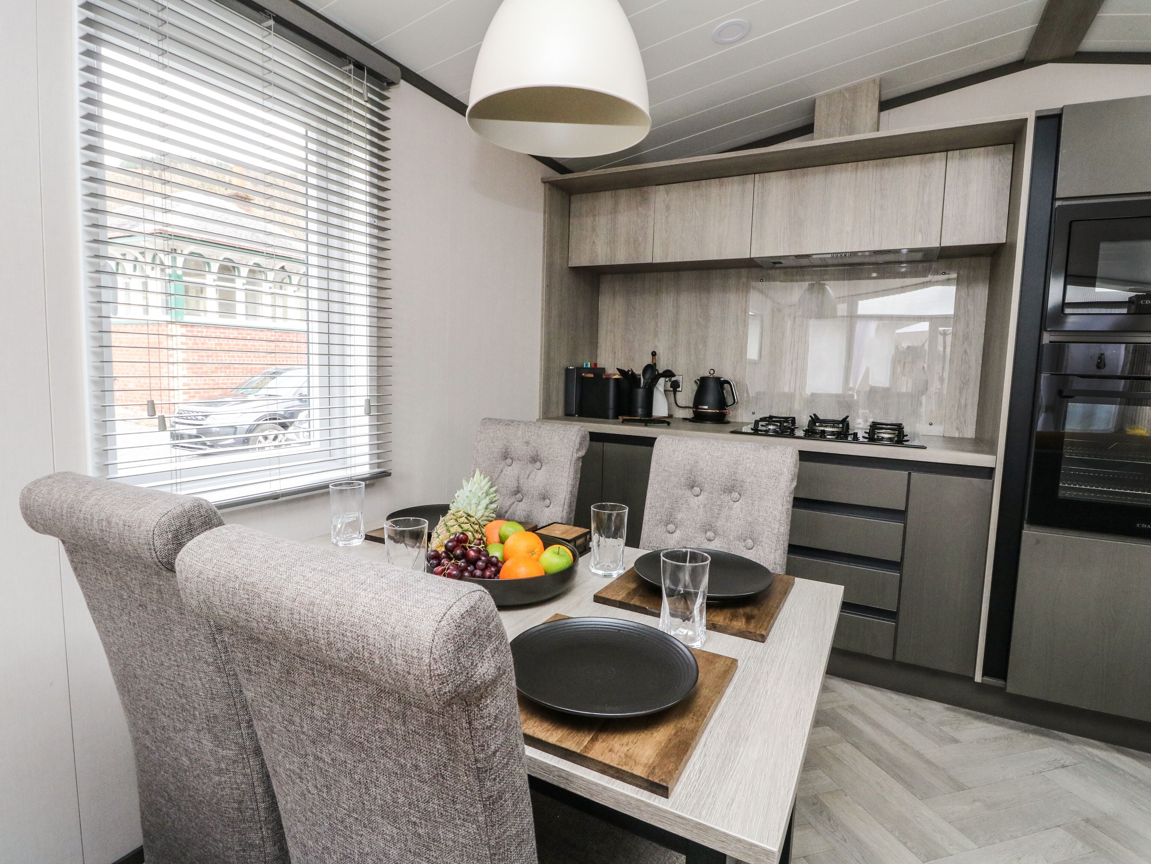 A modern kitchen with a dining area, featuring a table set for two with a fruit bowl, glasses, and plates.