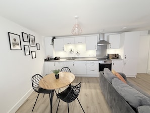 A modern kitchen with white cabinets, a dining table with chairs, a gray sofa, and a pendant light.