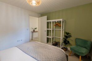 A bedroom with a bed, a green chair, a white shelving unit, and a hanging plant. - The Courtyard (Southampton)