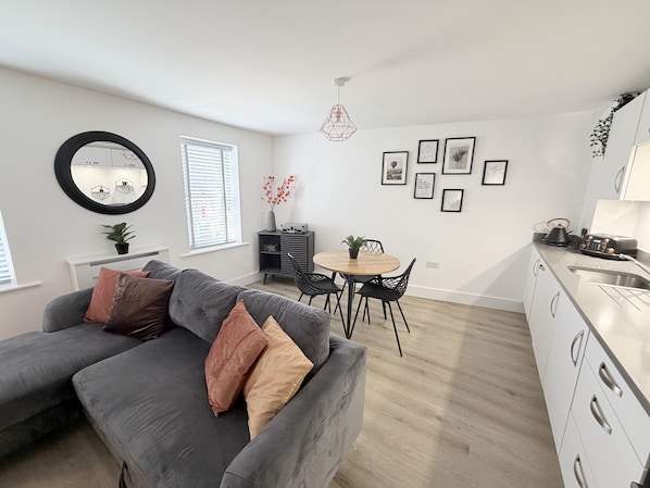 A modern apartment with a grey sofa, dining table, and kitchen area.