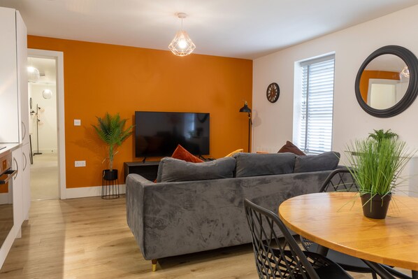 A modern living room with a grey sofa, a round wooden dining table, and two potted plants. - The Courtyard (Southampton)