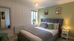 Et soveværelse med en stor seng, et natbord med lampe, et vindue med plante og et spejl på væggen.