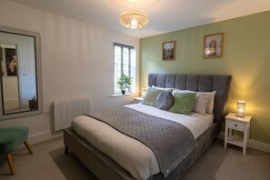 A bedroom with a large bed, a bedside table with a lamp, a window with a plant, and a mirror on the wall. - The Courtyard (Southampton)