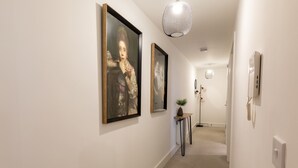 En gang med indrammede kunstværker på væggene, en potteplante på et sofabord og en moderne pendellampe.
