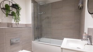 Et moderne badeværelse med en brusekabine med glasvægge, et hvidt toilet og en vask med sæbedispenser.