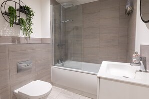 A modern bathroom with a glass-enclosed shower, a white toilet, and a sink with a soap dispenser. - The Courtyard (Southampton)
