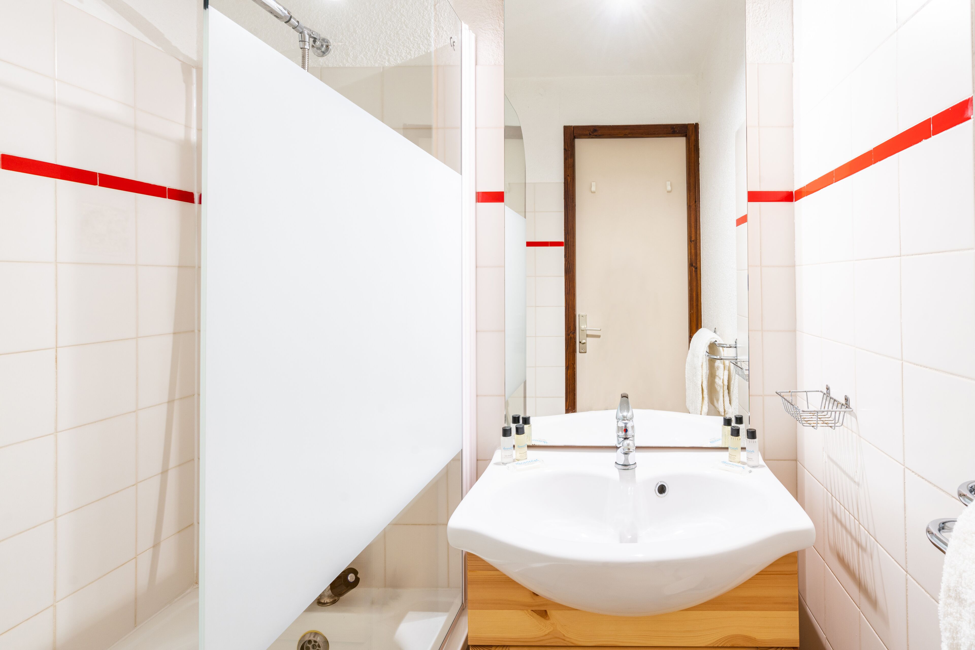 A modern bathroom with a white sink, wooden vanity, and a glass shower enclosure.