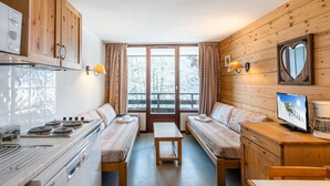 A cozy cabin-style room with wooden walls, a kitchenette, two beds with matching bedding, a television, and a window with curtains. - Vacancéole - Grand Morillon (Morillon)