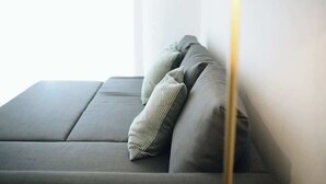 Un canapé moderne avec un coussin de couleur claire, adossé à un mur, un lampadaire à pied avec un pied doré et une fenêtre laissant entrer la lumière naturelle.