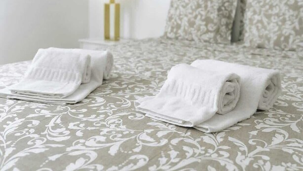 Un lit bien fait, recouvert d’une couvre-lit à motifs, avec deux serviettes blanches roulées posées dessus.