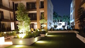 Une cour avec une pelouse artificielle, des plantes en pot et un chemin éclairé.
