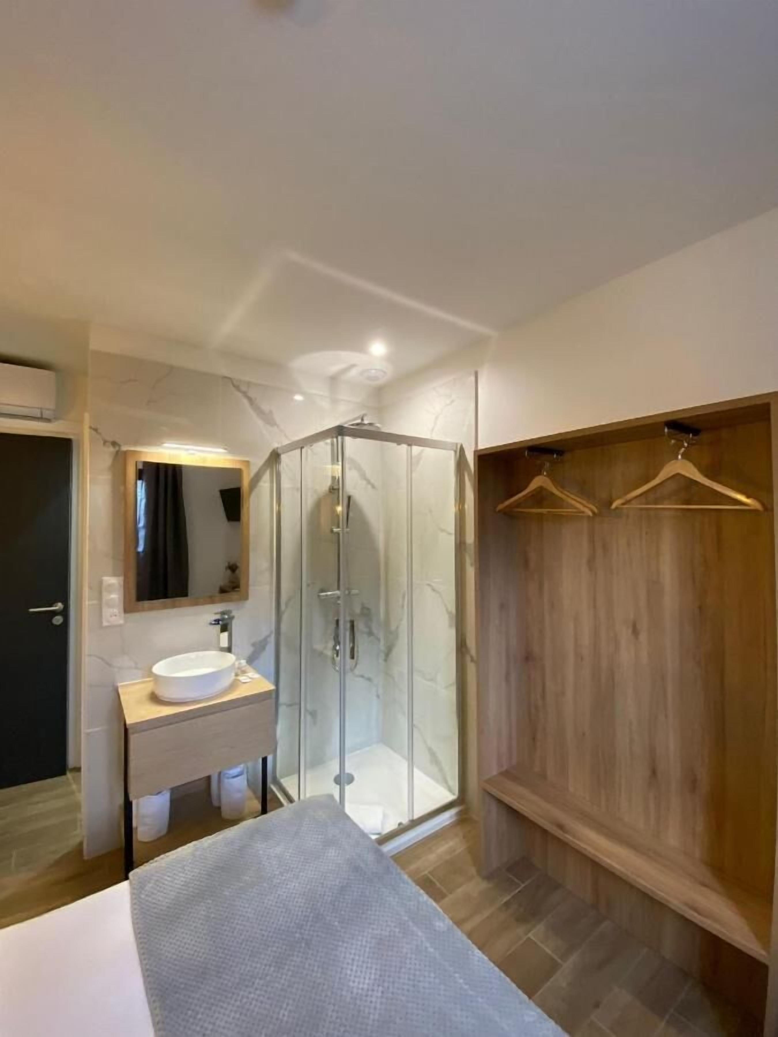 A modern bathroom with a glass shower enclosure, a wooden vanity, and a walk-in closet with wooden hangers.