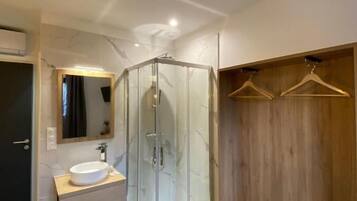 A modern bathroom with a glass shower enclosure, a wooden vanity, and a walk-in closet with wooden hangers.