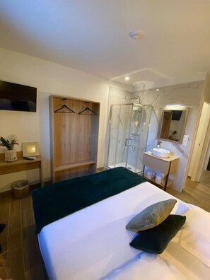 A modern hotel room with a bed, a walk-in closet, a shower, and a bathroom with a sink and mirror. - U Catagnu (San-Nicolao)