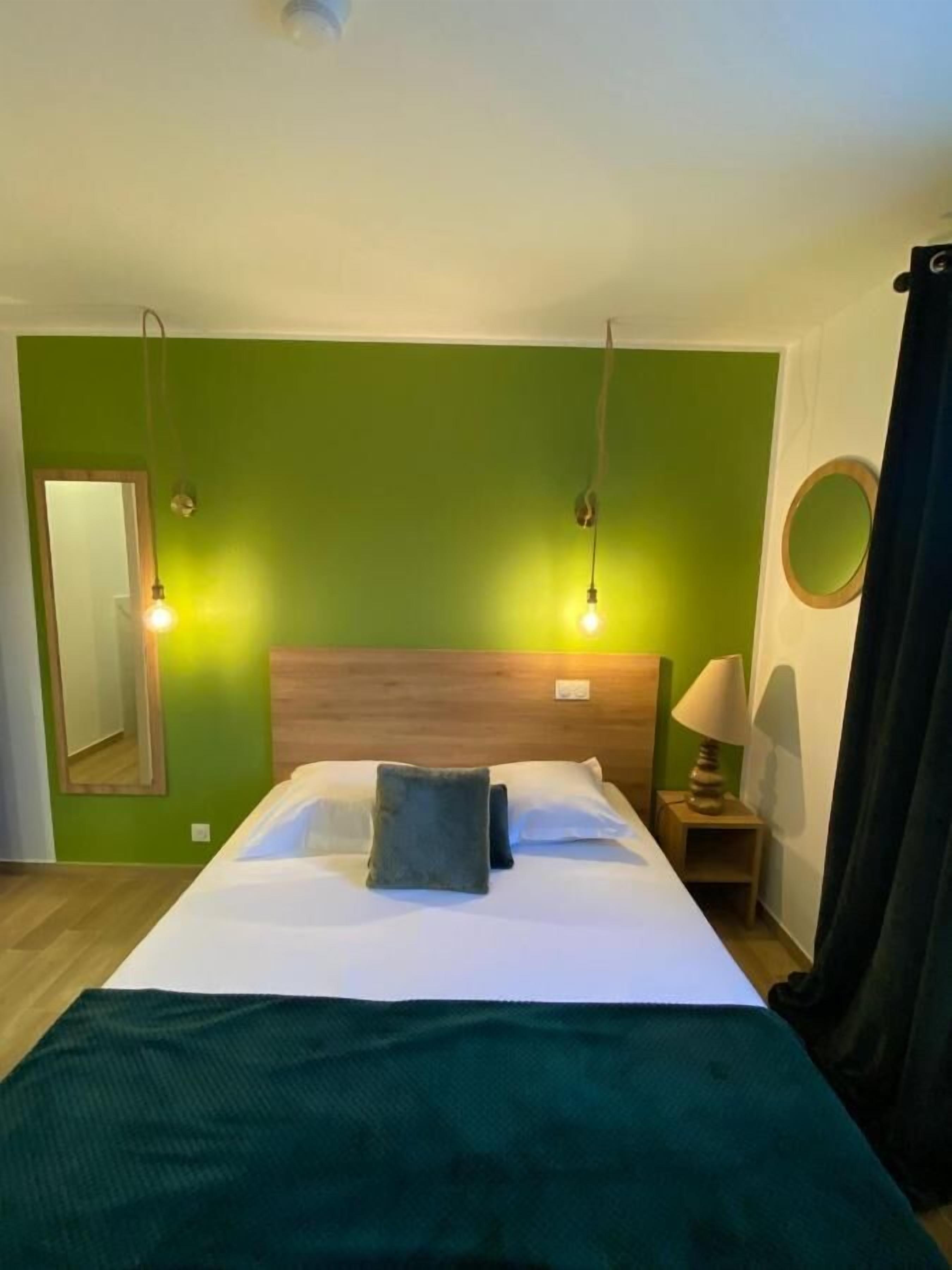 Quarto de hotel com uma cama grande, duas luminárias de cabeceira, uma mesa de cabeceira com luminária, um espelho e uma parede verde.
