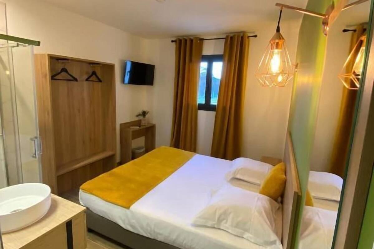 Ein Hotelzimmer mit Bett, Nachttisch, Spiegel, Kleiderschrank, Fernseher und einem Fenster mit Vorhängen.