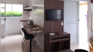 A modern kitchen with a built-in stove, a flat-screen TV, and a dining area with bar stools. - Jardins da Lagoa - Casas Completas (Caldas Novas)