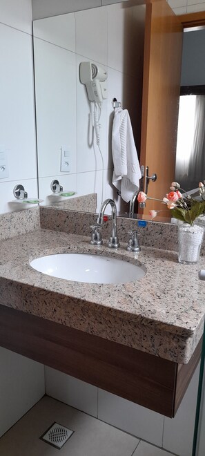 Een badkamer met een granieten aanrecht, een witte wastafel, een haardroger en een handdoekhouder.