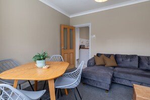 A cozy living room with a wooden dining table, grey upholstered sofa, and a potted plant. - The Hideout (Southampton)