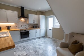 Une cuisine avec des armoires blanches, une hotte noire, un four à micro-ondes et un plan de travail en bois.