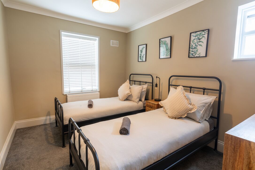 A bedroom with two single beds, a window with blinds, and wall-mounted artwork.