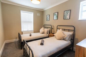 A bedroom with two single beds, a window with blinds, and wall-mounted artwork. - The Hideout (Southampton)