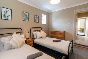 Une chambre avec deux lits, une tête de lit en bois, une table de chevet et des reproductions encadrées de motifs botaniques accrochées au mur.