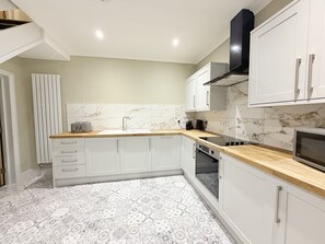 A modern kitchen with white cabinets, a marble backsplash, a wooden countertop, and a built-in oven.