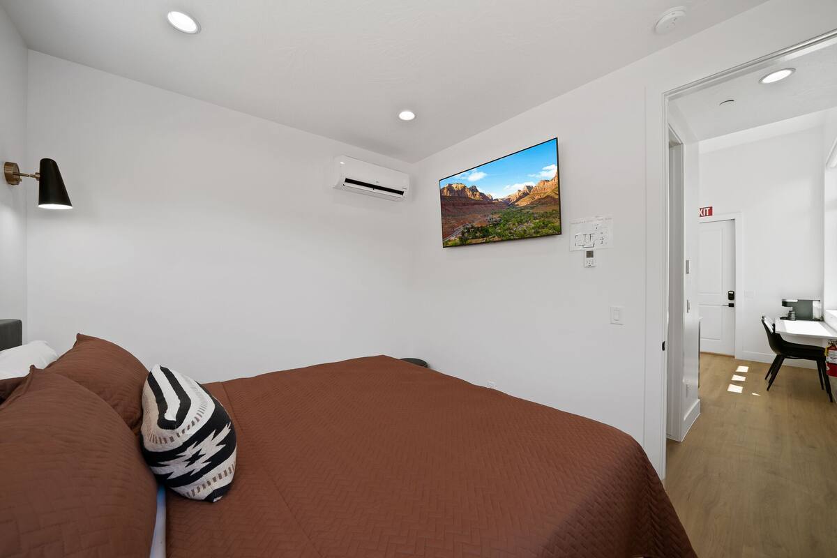 A bedroom with a large bed, a mounted TV, an air conditioning unit, and a door leading to a bathroom.