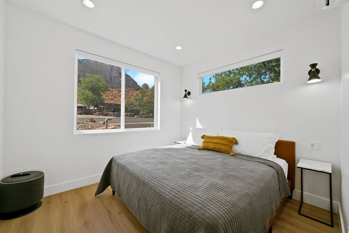 A bedroom with a large bed, a window with a mountain view, a small table, and a chair.