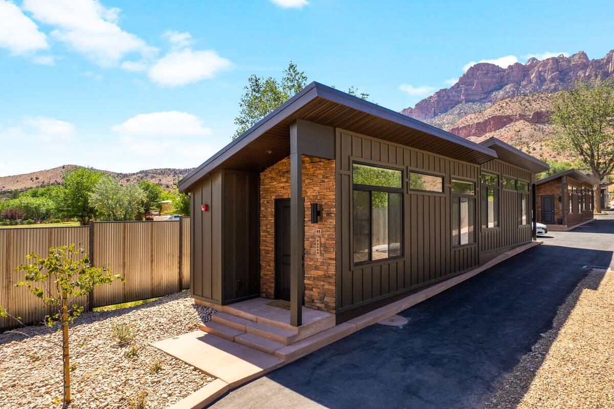 A modern building with a stone facade and large windows, set against a mountainous backdrop.