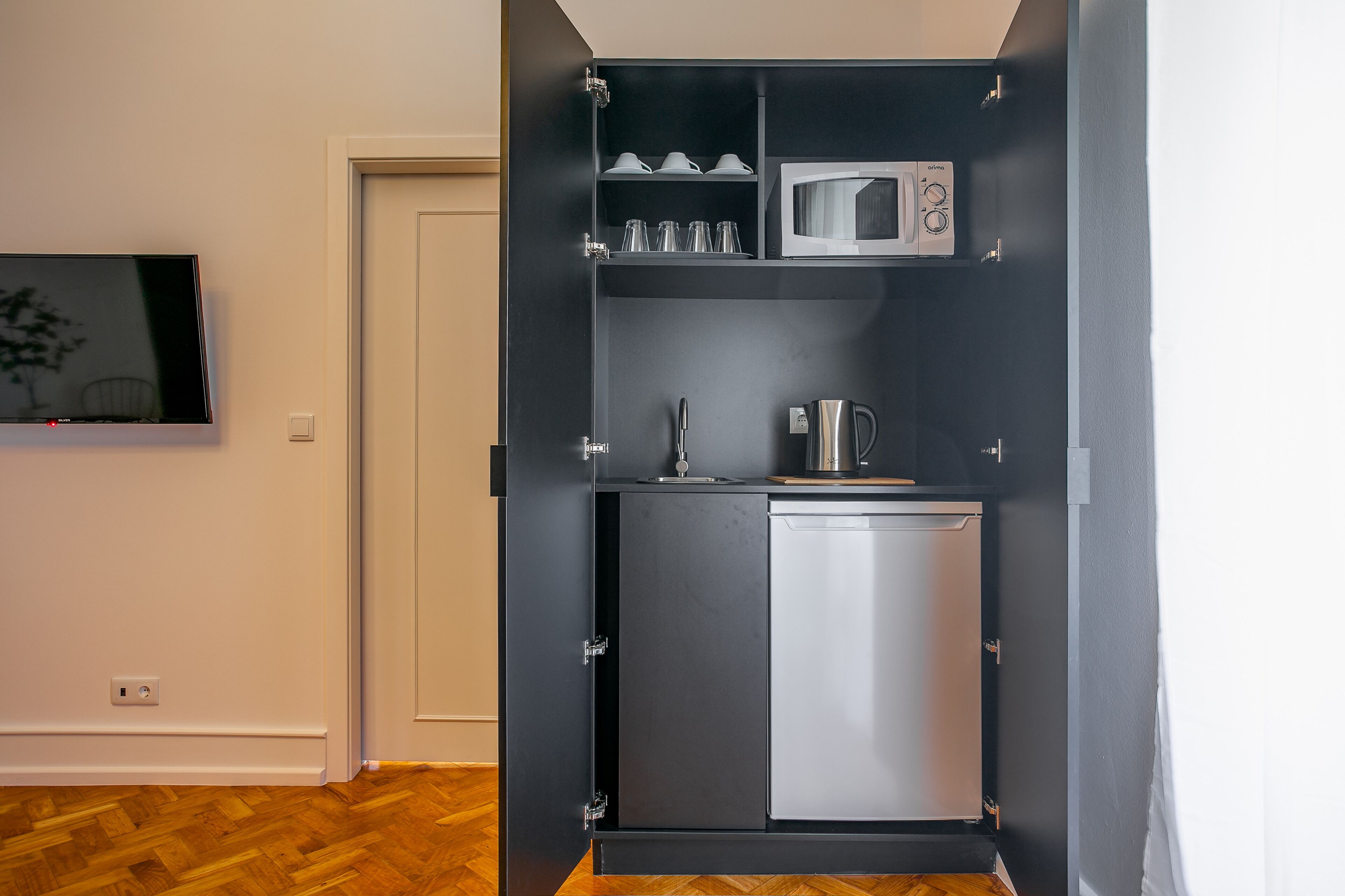 Una kitchenette compacta con microondas, un lavamanos pequeño y un armario con vajilla.