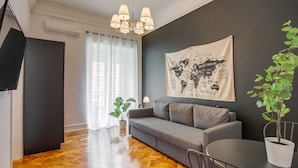 A modern living room with a grey sofa, a wooden herringbone floor, a world map on the wall, and a potted plant. - Home Out 1E - 5 Bedroom Apartament with Parking (Lisboa)