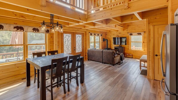 Interior de una cabaña de madera con comedor, cocina y un altillo.