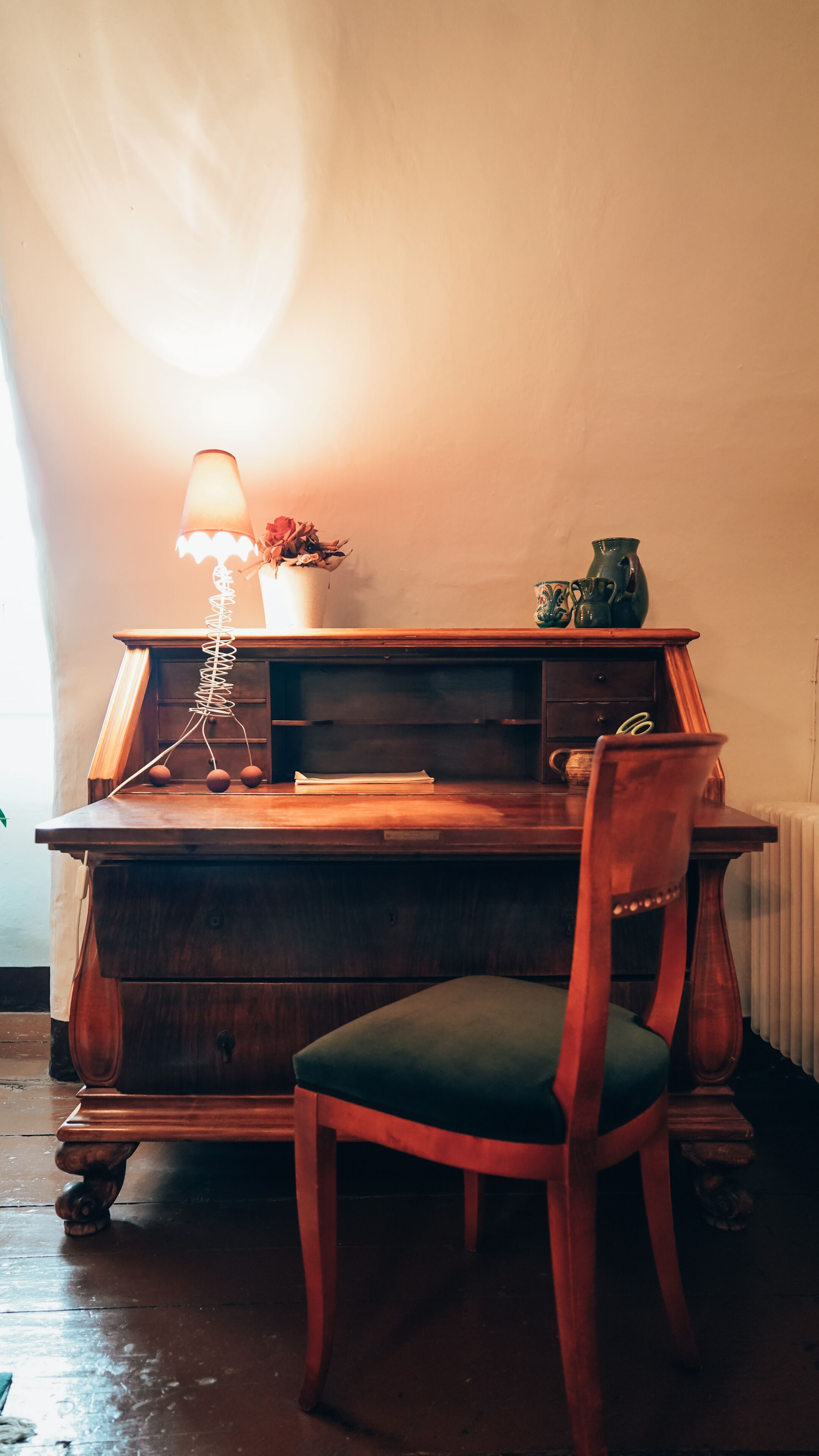 Un bureau en bois, une lampe, une chaise et un vase rempli de fleurs.