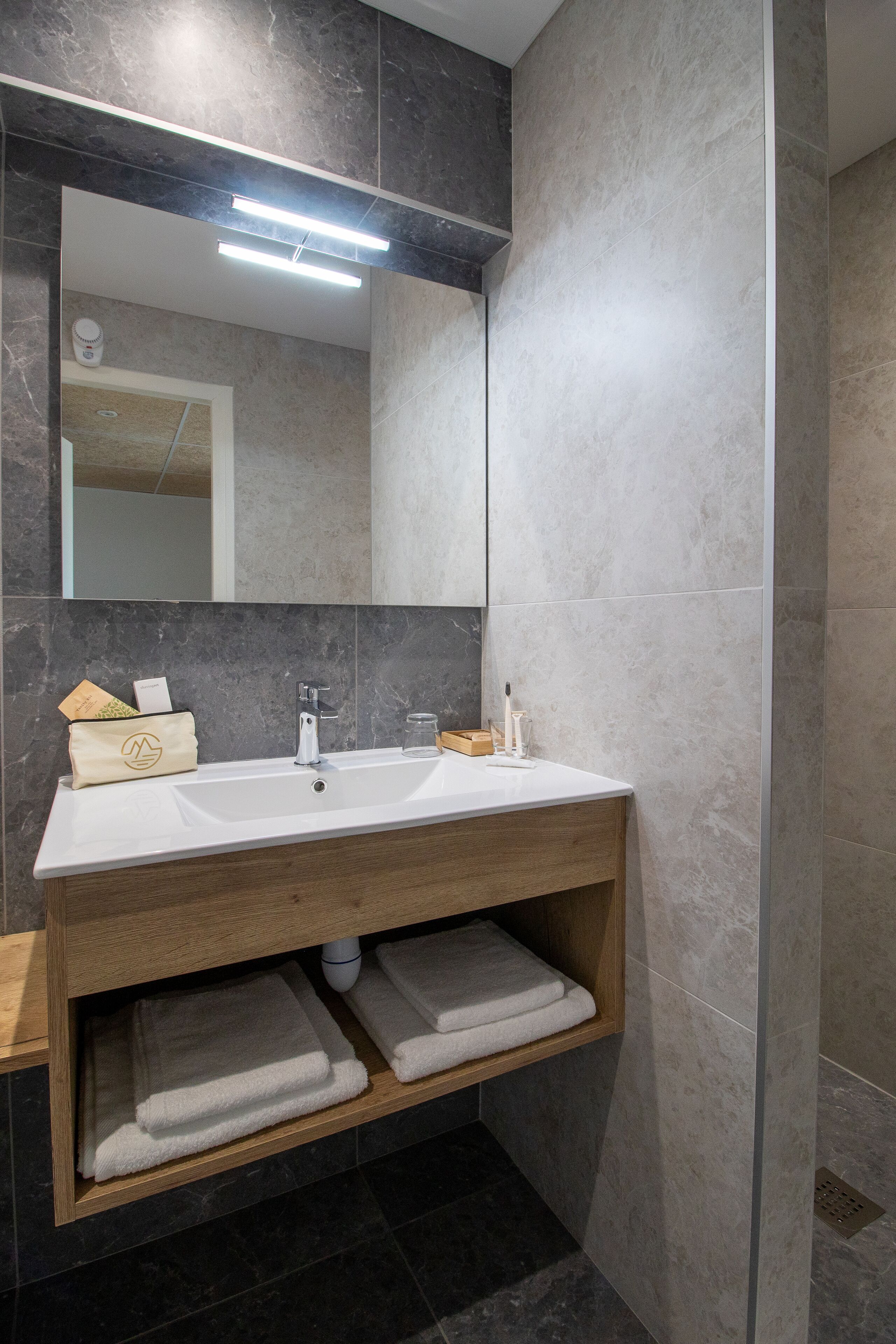 Un baño moderno con lavamanos blanco, tocador de madera y espejo.