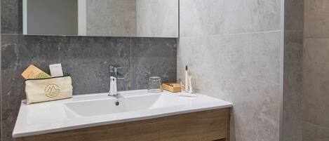 Un baño moderno con lavamanos blanco, tocador de madera y espejo.