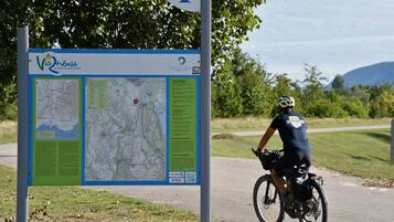 A map sign with text and a QR code, a cyclist on a path, and a natural landscape with trees and hills.