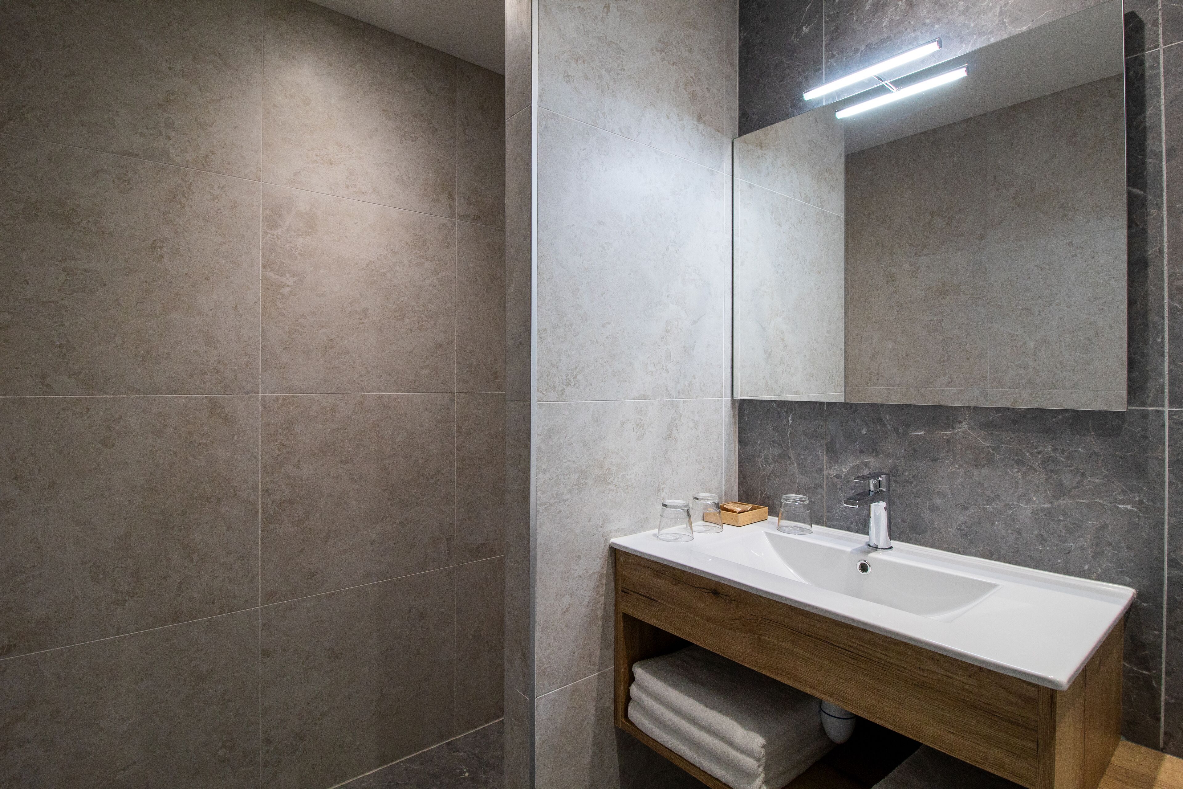 A modern bathroom with a large mirror, a white sink, and a wooden vanity.