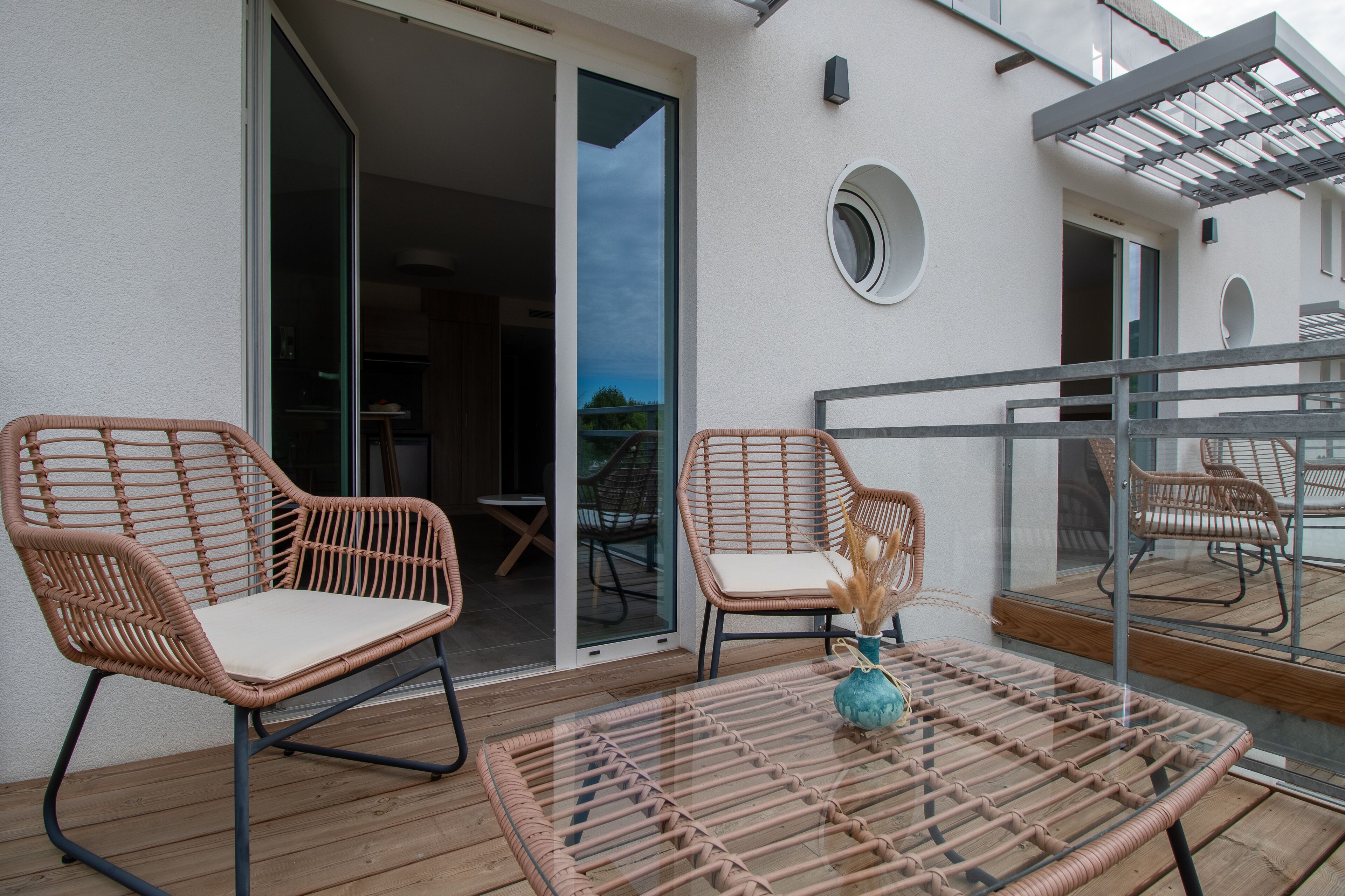 Een balkon met rieten stoelen, een glazen tafel en een schuifpui, met uitzicht op de lucht.