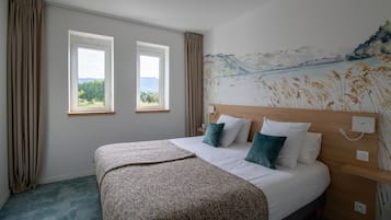 Ein Schlafzimmer mit einem großen Bett, zwei Fenstern, einem Bild an der Wand und einem Nachttisch.