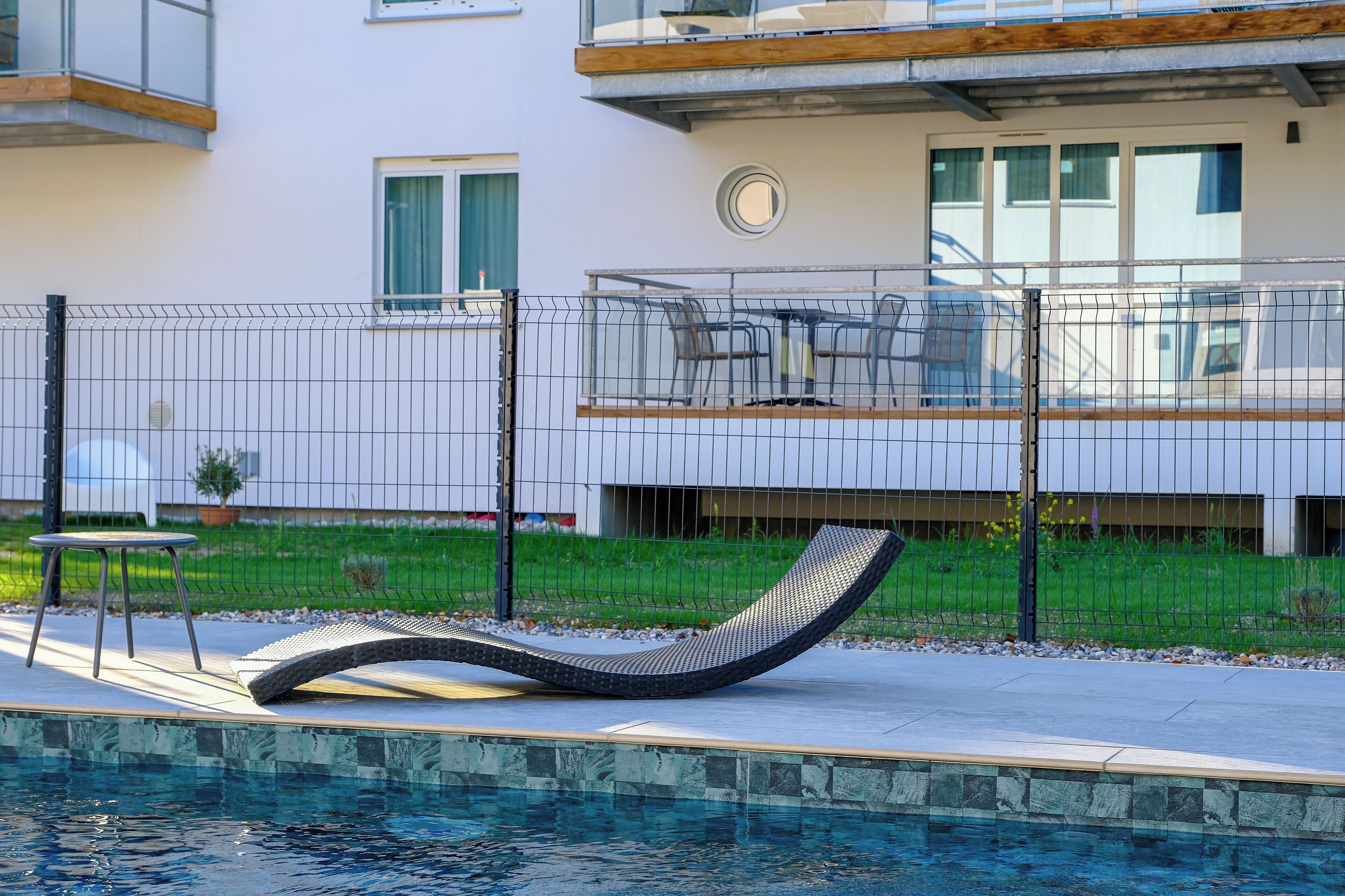 A modern outdoor pool area with a lounge chair, a small table, and a fence.